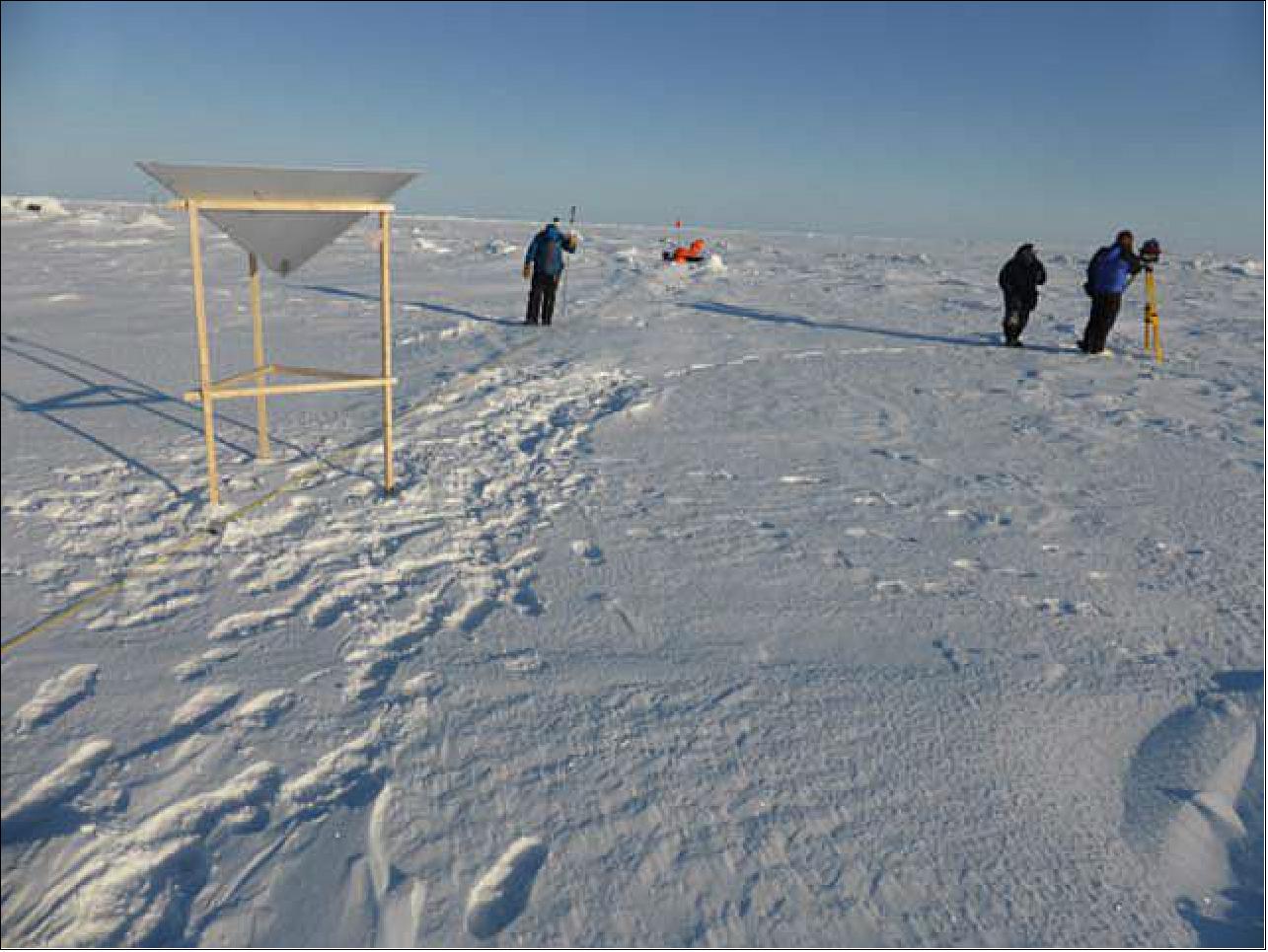 Figure 27: Ground measurements at Camp 2 in the Beaufort Sea. Photo shows Eastern corner reflector, Magnaprobe snow thickness measurement, row of orange garbage bags (background), and terrestrial laser scanner (image credit: YU)