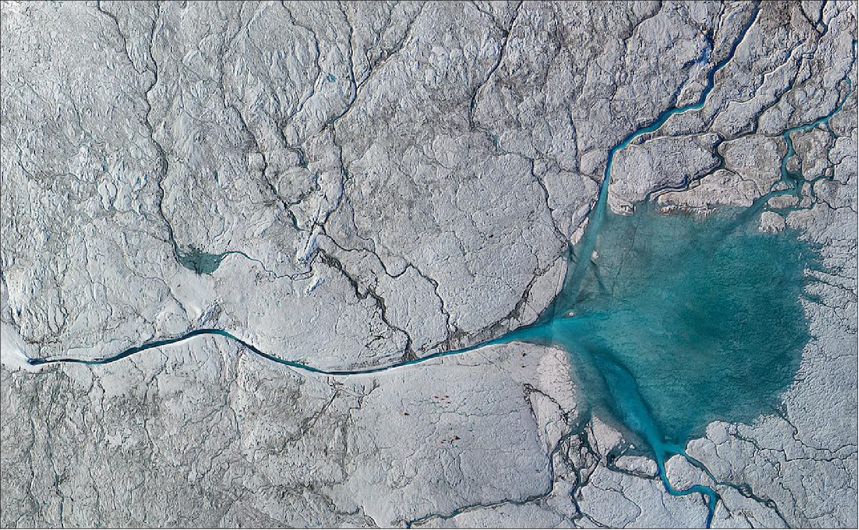 Figure 11: At the fringes of the Greenland Ice Sheet, where glaciers are constantly melting, water rushes everywhere through an intricate system of lakes and streams that branch out like slip and slide shoots of super chilled, bright turquoise water. Some of that water eventually cascades straight into the surrounding land and ocean through channels and cracks. Some of it thunders off into sinkhole-like structures on the ice called moulins. Rumbling 24 hours a day, these holes swallow water from the surface and funnel it to the bedrock at the base of the ice (credit: image courtesy of Dr. Laurence C. Smith)