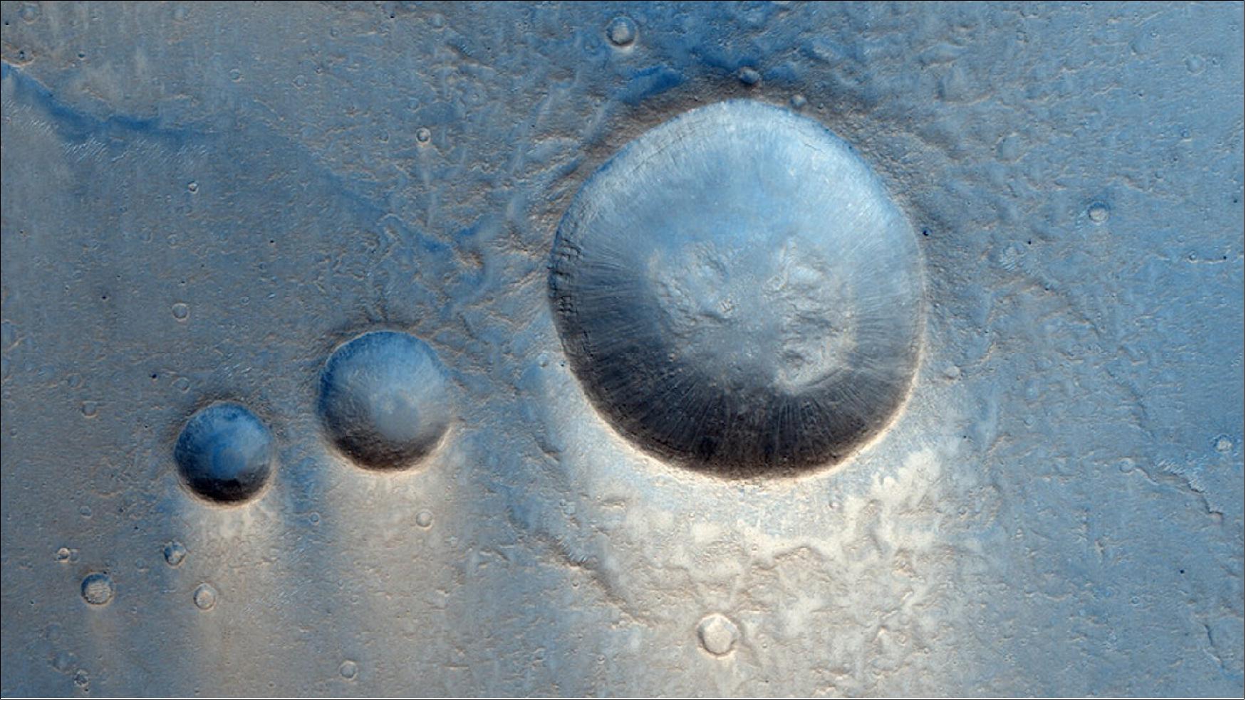 Figure 22: This Mars region is known to be covered by large lava deposits probably from the nearby Tharsis Montes volcanoes. In this image three medium-sized impact craters take center stage, with many smaller impacts pockmarking the scene. Zooming into the larger craters it is possible to see layers in the inner rim that could represent the successive accumulation of lava flows in this area (image credit: ESA/Roscosmos/CaSSIS, CC BY-SA 3.0 IGO)