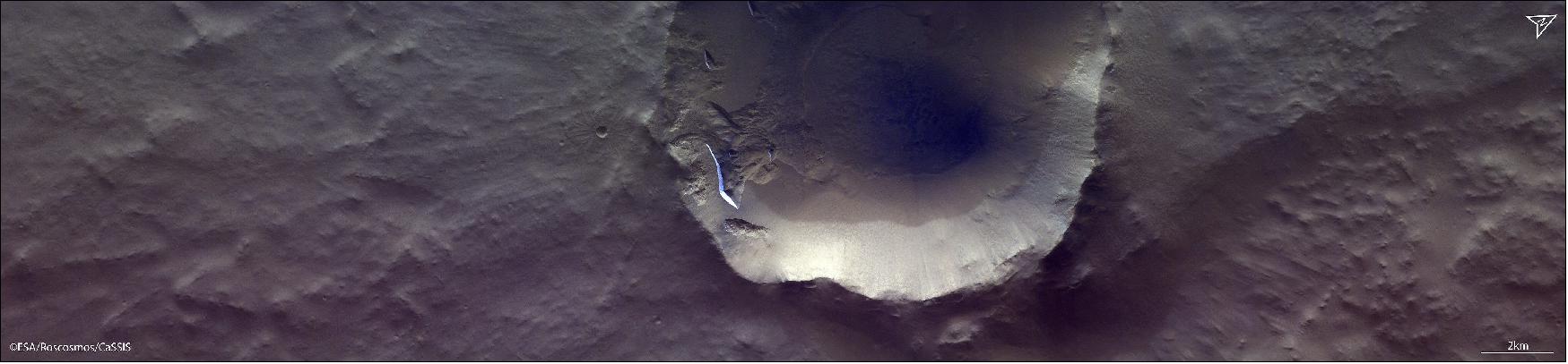 Figure 16: Despite the low light in this late evening image, several north-facing icy scarps are distinctly visible because of their covering of bright white carbon dioxide frost. The frost disappears in spring, but remains late on these scarps because of their pole-facing orientation. - This 11 km diameter crater is located in the northern plains of Mars at 55º16'51.6"N/106º25'3.4"W, north of Alba Mons (image credit: ESA/Roscosmos/CaSSIS, CC BY-SA 3.0 IGO)