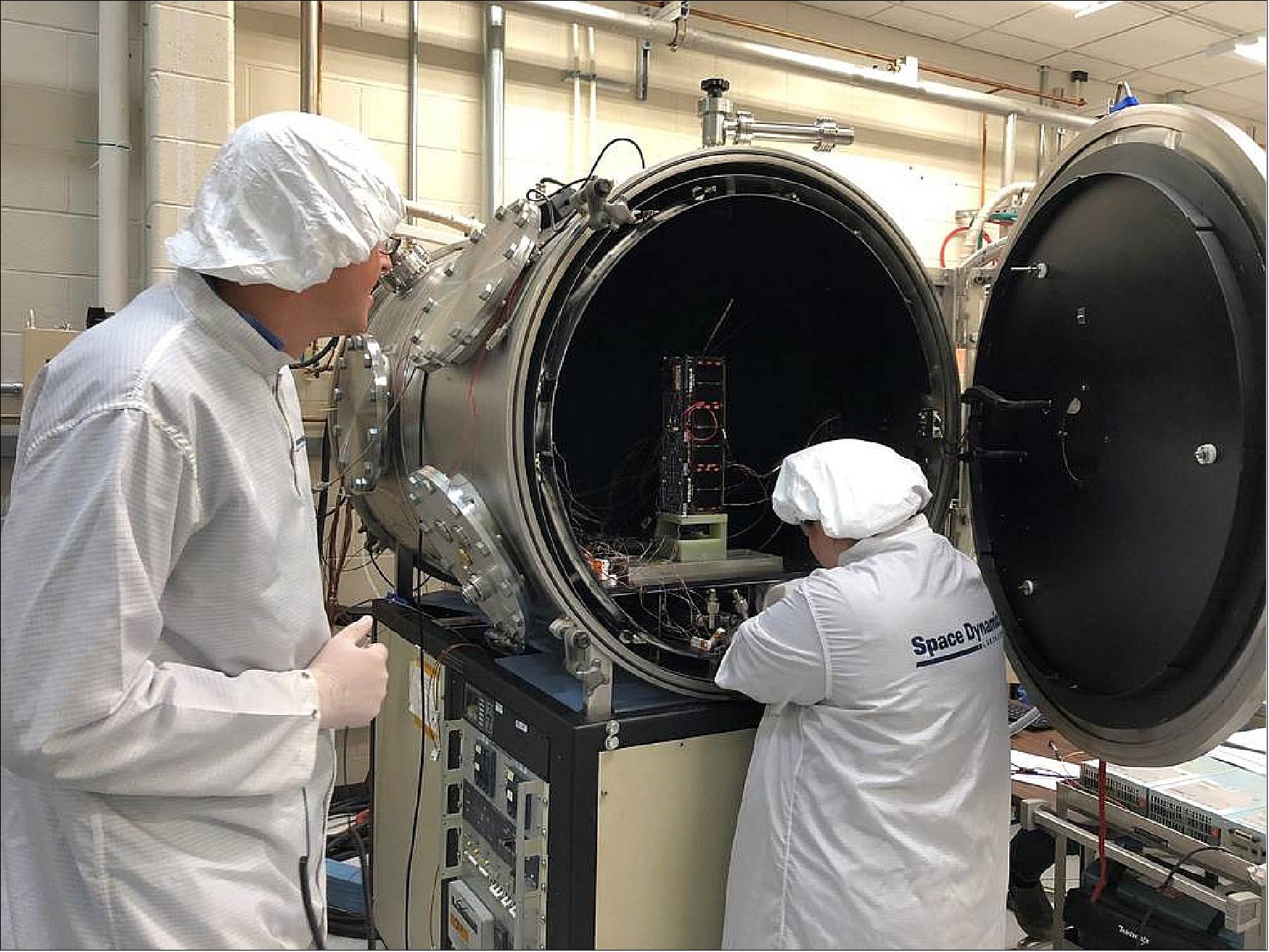 Figure 3: HARP Systems Engineer Ryan Martineau (left) and Thermal Vacuum Specialist Brittany Woytko configure HARP’s spacecraft in a thermal vacuum chamber at the Space Dynamics Laboratory in Logan, Utah. Woytko is connecting several temperature sensors to the spacecraft to monitor the instrument during testing. Once the door is shut on the chamber, it loses its air and simulates the vacuum of space. The chamber also heats and cools the spacecraft through several cycles to simulate the extreme hot and cold temperatures the spacecraft will pass through on orbit (image credit: USU/SDL) 5)