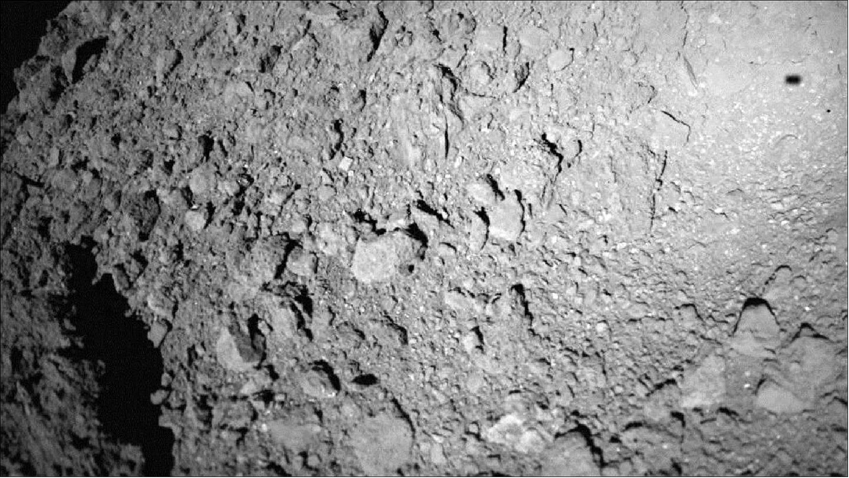 Figure 83: Shadow of MASCOT on asteroid Ryugu during descent: DLR's MasCam on board MASCOT acquired this image as it descended to the the asteroid Ryugu 3.5 minutes after separating from its mothercraft Hayabusa-2. In the image, the lander is ~20 m above the asteroid's surface, and MASCOT's shadow can be seen at the top right (image credit: MASCOT/DLR/JAXA)