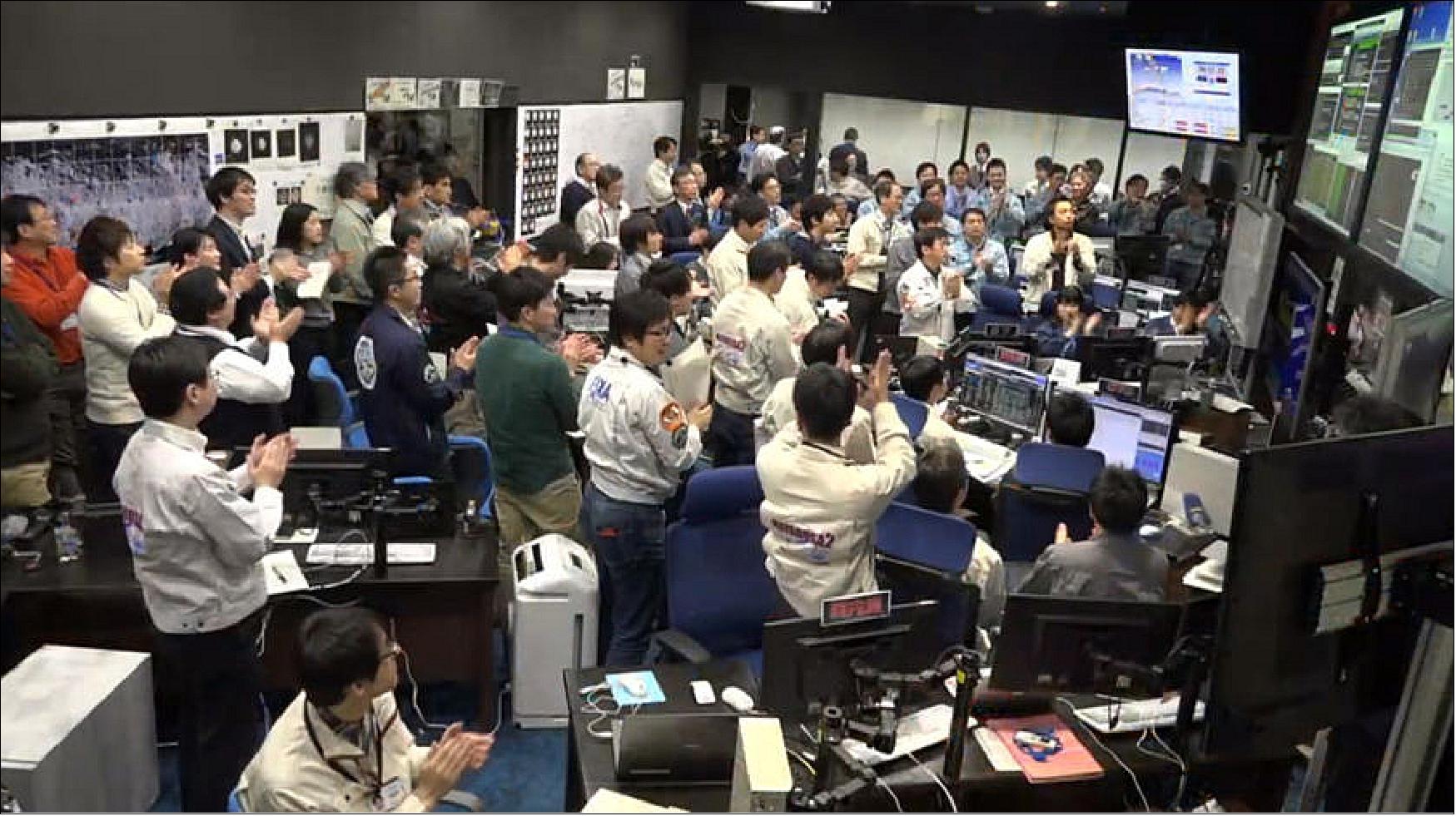Figure 65: Celebration in Hayabusa-2 mission control room after successful touchdown on Ryugu. A packed control room celebrates a subtle shift in Hayabusa-2's radio signal, marking the moment of its touchdown and sample grab on Ryugu on 21 February 2019 at 22:49 UTC (image credit: JAXA)