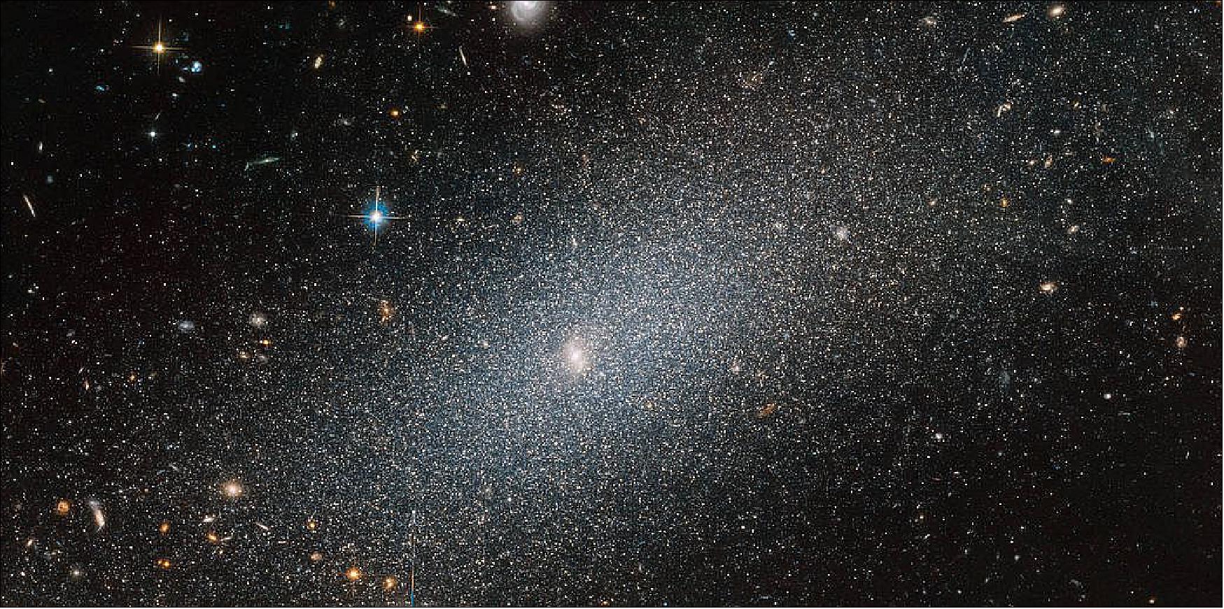 Figure 48: This spotlight-hogging galaxy, seen set against a backdrop of more distant galaxies of all shapes and sizes, is known as PGC 29388. Although it dominates in this image, this galaxy is a small player on the cosmic stage and is known as a dwarf elliptical galaxy. As the “dwarf” moniker suggests, the galaxy is on the smaller side, and boasts a “mere” 100 million to a few billion stars — a very small number indeed when compared to the Milky Way's population of around 250 billion to 400 billion stellar residents (image credit: ESA/Hubble & NASA, T. Armandroff)