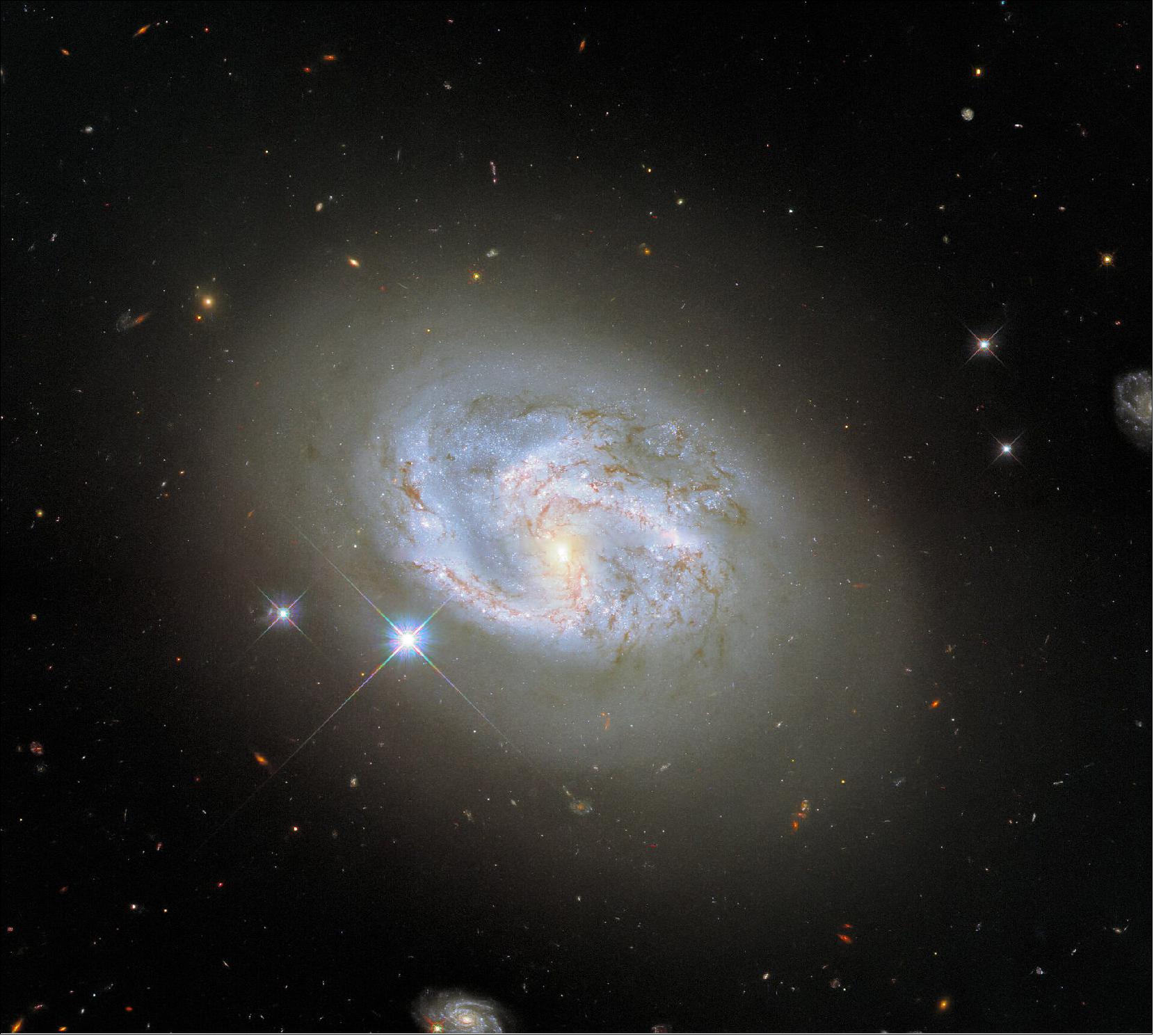 Figure 79: NGC 4680 is actually a rather tricky galaxy to classify. It is sometimes referred to as a spiral galaxy, but it is also sometimes classified as a lenticular galaxy. Lenticular galaxies fall somewhere in between spiral galaxies and elliptical galaxies. Whilst NGC 4680 does have distinguishable spiral arms, they are not clearly defined, and the tip of one arm appears very diffuse. Galaxies are not static, and their morphologies (and therefore their classifications) vary throughout their lifetimes. Spiral galaxies are thought to evolve into elliptical galaxies, most likely by merging with one another, causing them to lose their distinctive spiral structures (image credit: ESA/Hubble & NASA, A. Riess et al.; CC BY 4.0)