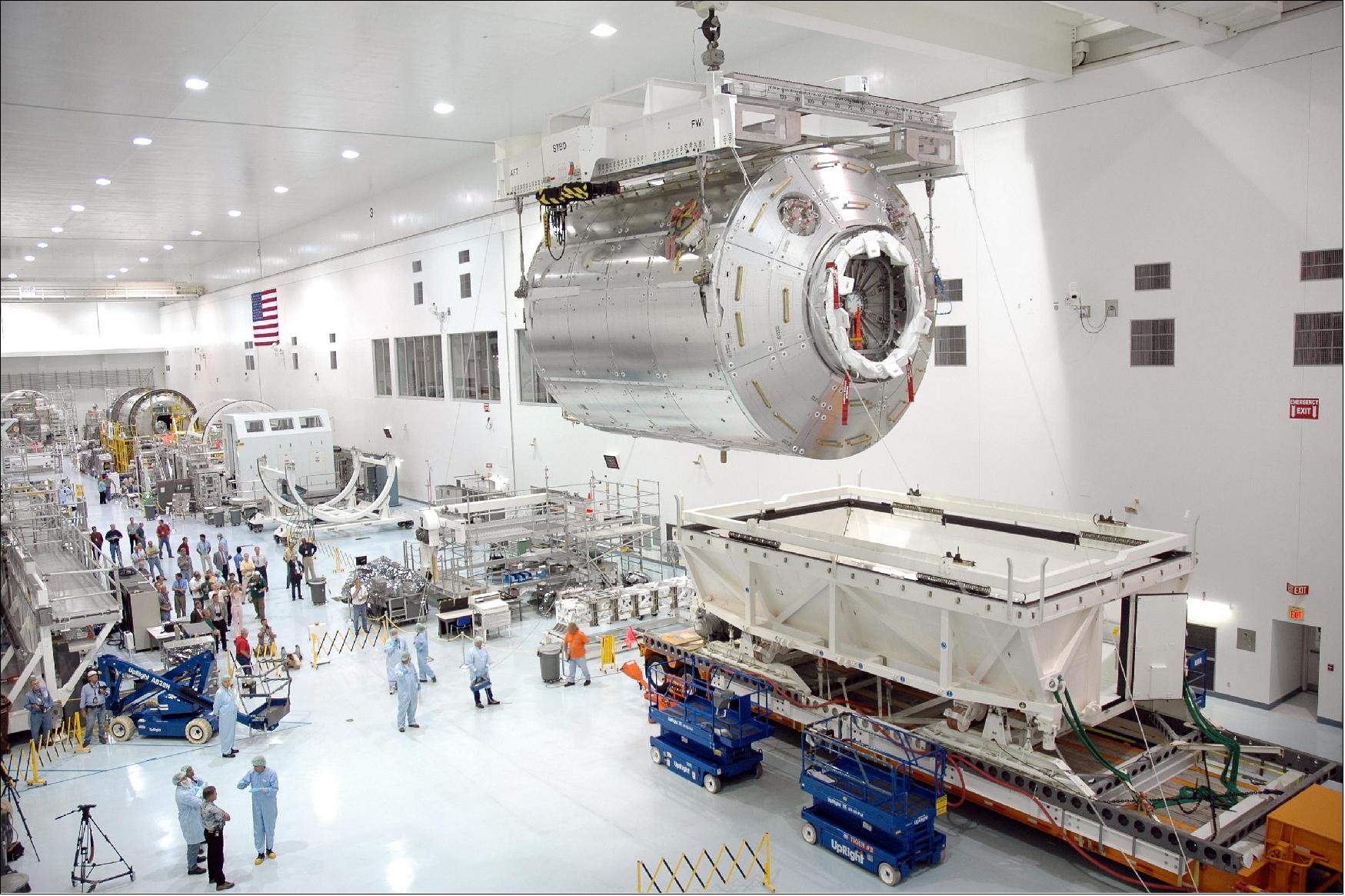 Figure 14: Columbus to scale. The focus of this image is the suspended European Columbus module being moved onto a work stand in a cleanroom at the Kennedy Space Center in Florida, USA. Of course, a cylindrical module of more than 10 t (without payloads) for housing laboratory equipment, storage units and three working astronauts is big, but the contrast between Columbus and the people in the image is startling. Even more so when we remember that Columbus is one of 16 similarly sized modules orbiting 400 km over our heads (image credit: NASA)