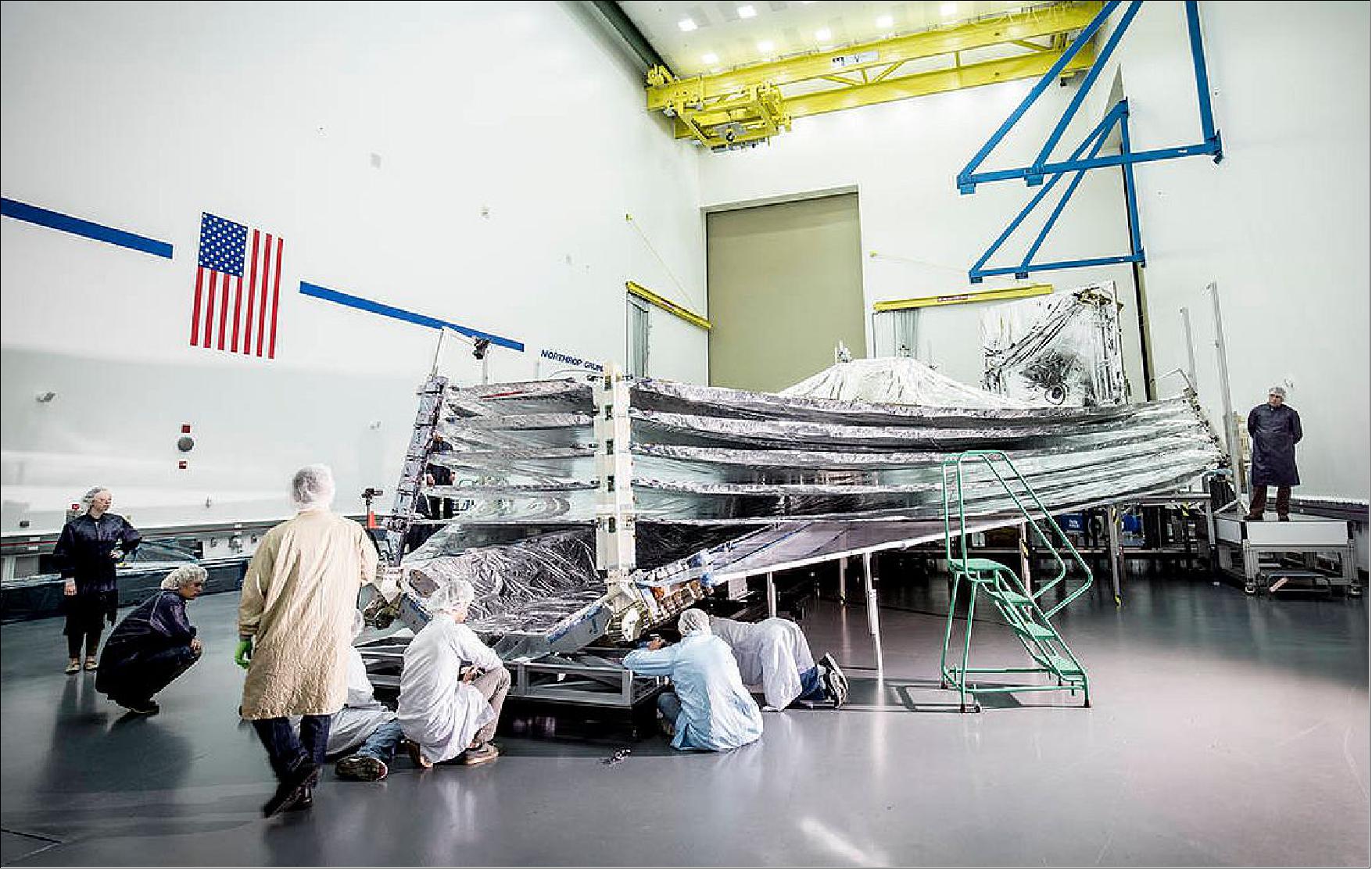 Figure 66: In this photo, engineers and scientists examine the sunshield layers on this full-sized test unit. Because there's a layer of the shiny silver material on the base under the five layers of the sunshield, it appears as if the sunshield has a mouth that is "open wide" while engineers take a look. The photo was taken in a clean room at Northrop Grumman Corporation, Redondo Beach, California.. (image credit: NASA)