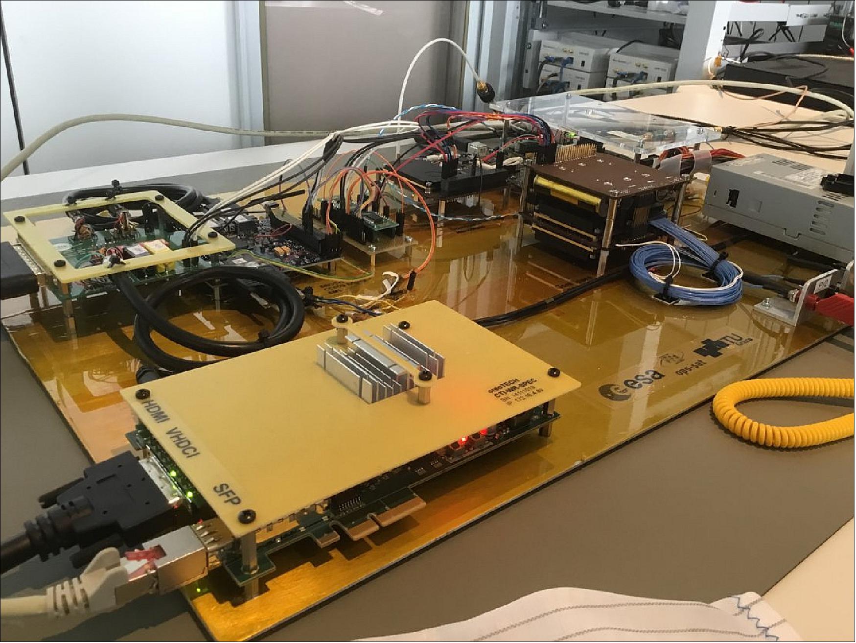 Figure 11: Photo of the OPS-SAT engineering model on a test bench gets connected to an innovative ground control system at ESA/ESOC for the first time (image credit: ESA, CC BY-SA 3.0 IGO)